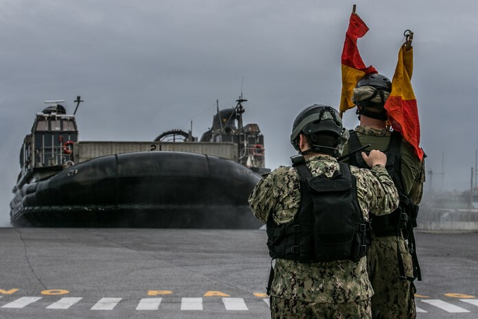 U.S. Navy ET2 Paul Saldana, left, electronics technician, and CM2 Adam Long, construction mechanic, both with Naval Beach Unit 7, conduct ramp marshall duties to guide a Landing Craft Air Cushion into port on Naval Base White Beach, Okinawa, Japan, June 1, 2021. Marines from 3d MLG and Sailors from NBU-7 integrated to load and transport personnel and equipment in support of exercise Poseidon’s Watchtower. NBU-7 is an operational, forward deployed unit that directly contributes to the core capabilities of U.S. Maritime Sea Power by facilitating the movement of troops, equipment, vehicles and supplies from amphibious shipping across the beach. 3d MLG, based out of Okinawa, Japan, is a forward deployed combat unit that serves as III MEF’s comprehensive logistics and combat service support backbone for operations throughout the Indo-Pacific area of responsibility. Saldana is a native of Miramar, Florida, and Long is a native of Sanford, North Carolina.