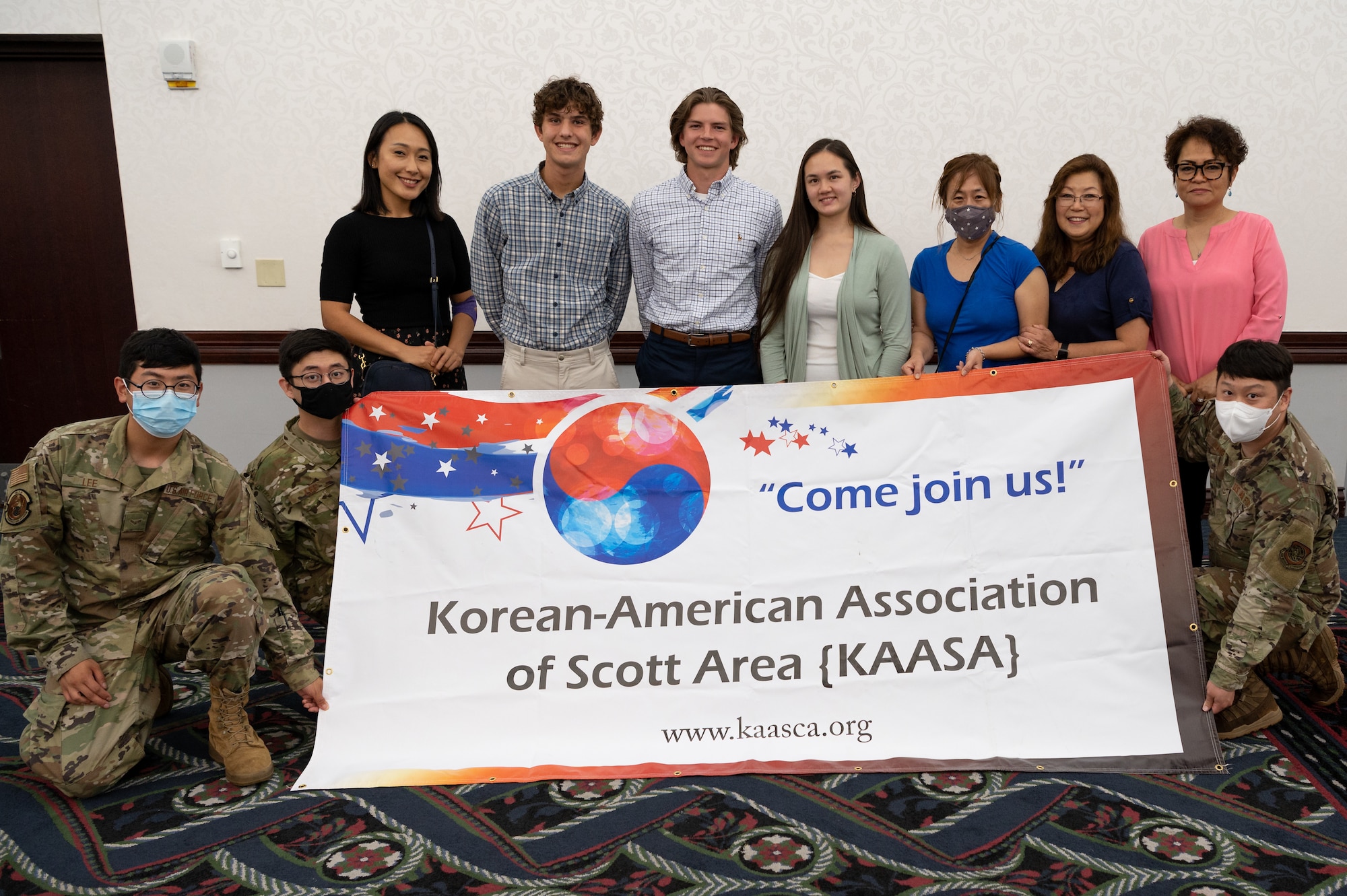 U.S. Air Force Members, and local high school students gather around a Korean American Association of Scott Area banner after being awarded scholarships on Scott Air Force Base, Illinois, May 27, 2021. KAASA is a non-profit private organization that supports the local community through charity and educational outlets, and through donations they awarded $1,000 scholarships to students Danielle Chao, Alex Tillock, and Brady Martinez. (U.S. Air Force Photo by Airman 1st Class Isaac Olivera)