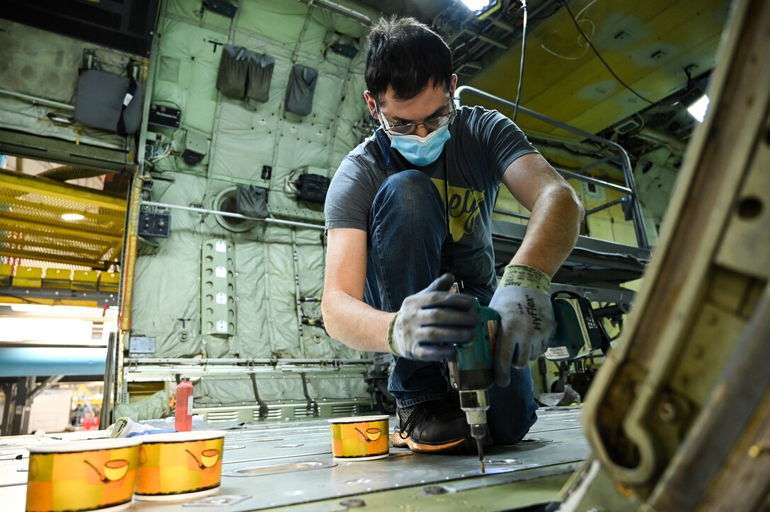 A maintainer uses a drill inside a C-130.