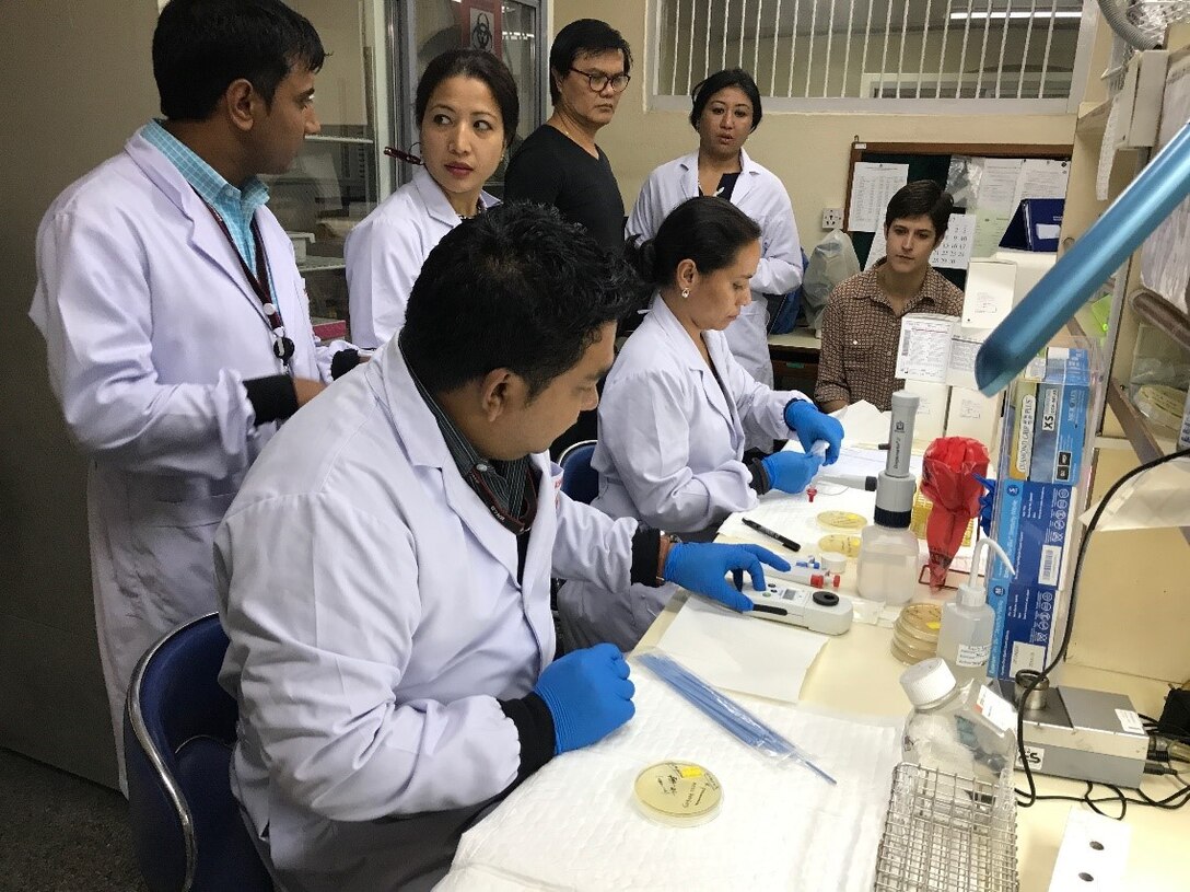 Scientists in lab coats working at a table with petri dishes.