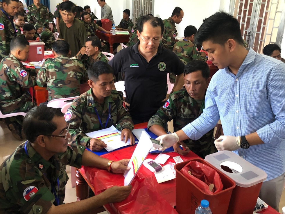 One scientist in civilian clothes teaching uniformed Soldiers about how to use a rapid diagnostic test.