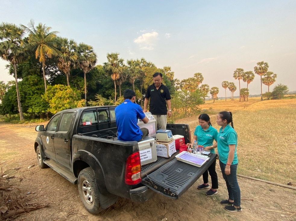 Four scientists setting up a mobile malaria screening laboratory from the back of a pickup truck.