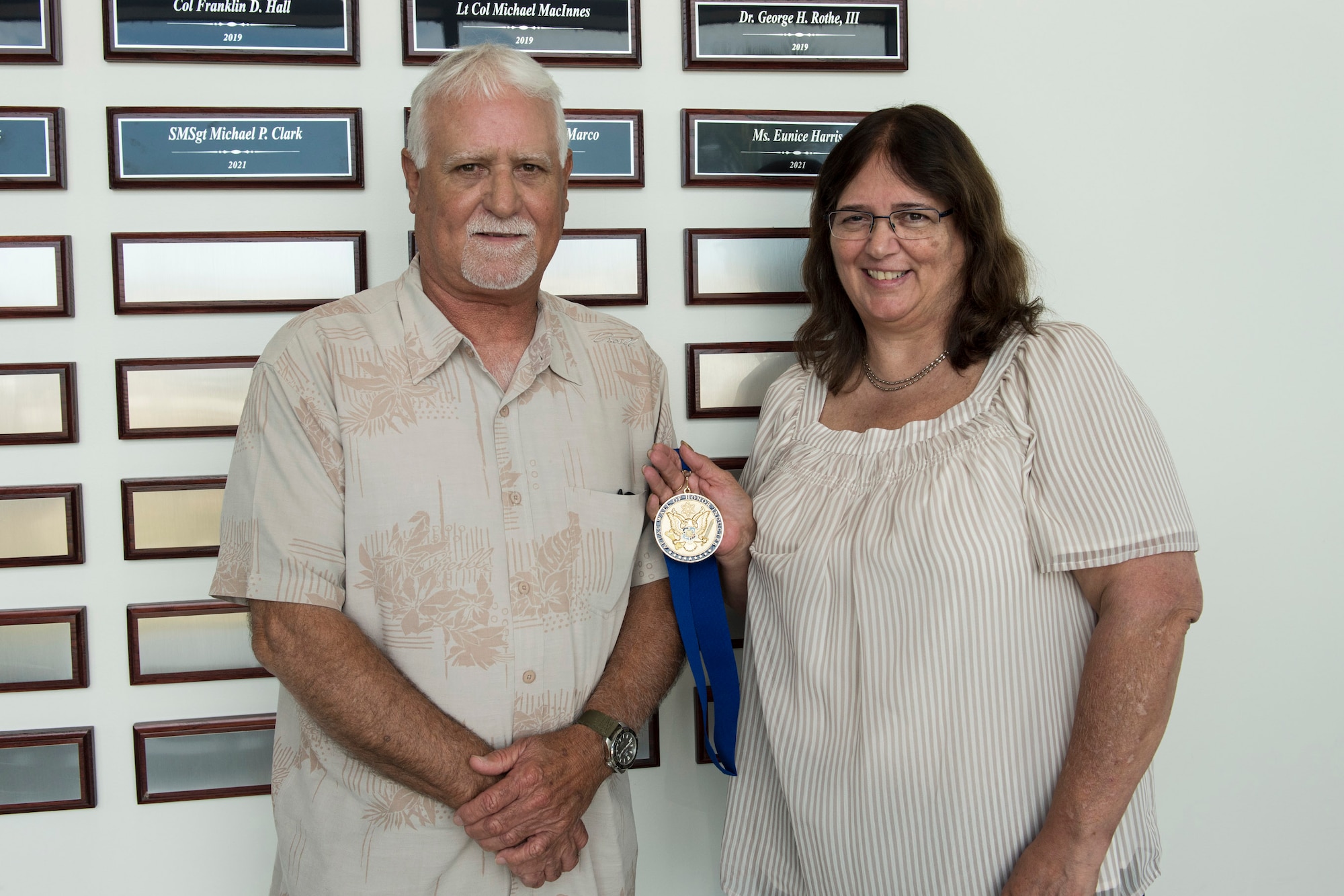 Mike Harris and his sister Tina Colon, children of Ms. Eunice Harris, pose with their mother's medallion after she was posthumously inducted into the Air Force Technical Applications Center's Wall of Honor May 26, 2021.  Harris served more than 31 years in civil service, with 20 of those years as the administrative assistant to AFTAC's senior scientist at the Department of Defense's sole nuclear treaty monitoring center.  (U.S. Air Force photo by Matthew S. Jurgens)