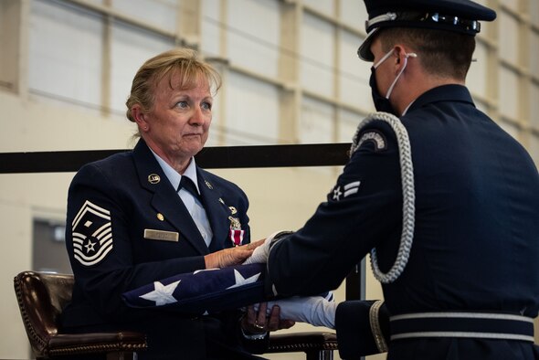 Honor guardsman hands folded American flag to crying female Airman.