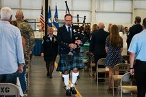 Man in kelt leads woman down aisle while playing bagpipes.