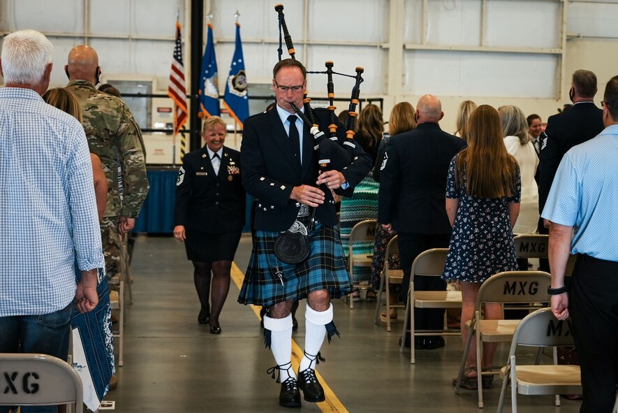 Man in kelt leads woman down aisle while playing bagpipes.