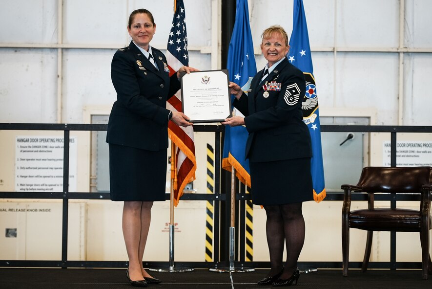Two women in dress blues hold a certificate on a stage.