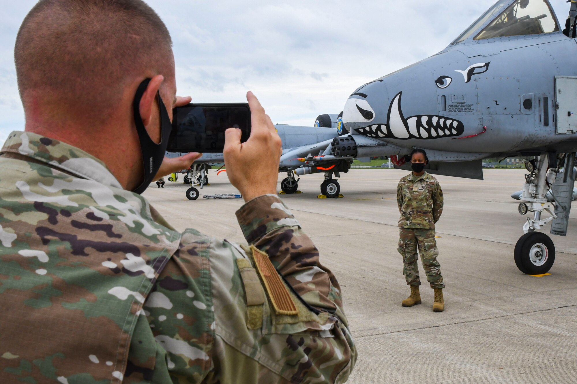 A photo of an airmen taking a picture of another airman in front of a jet