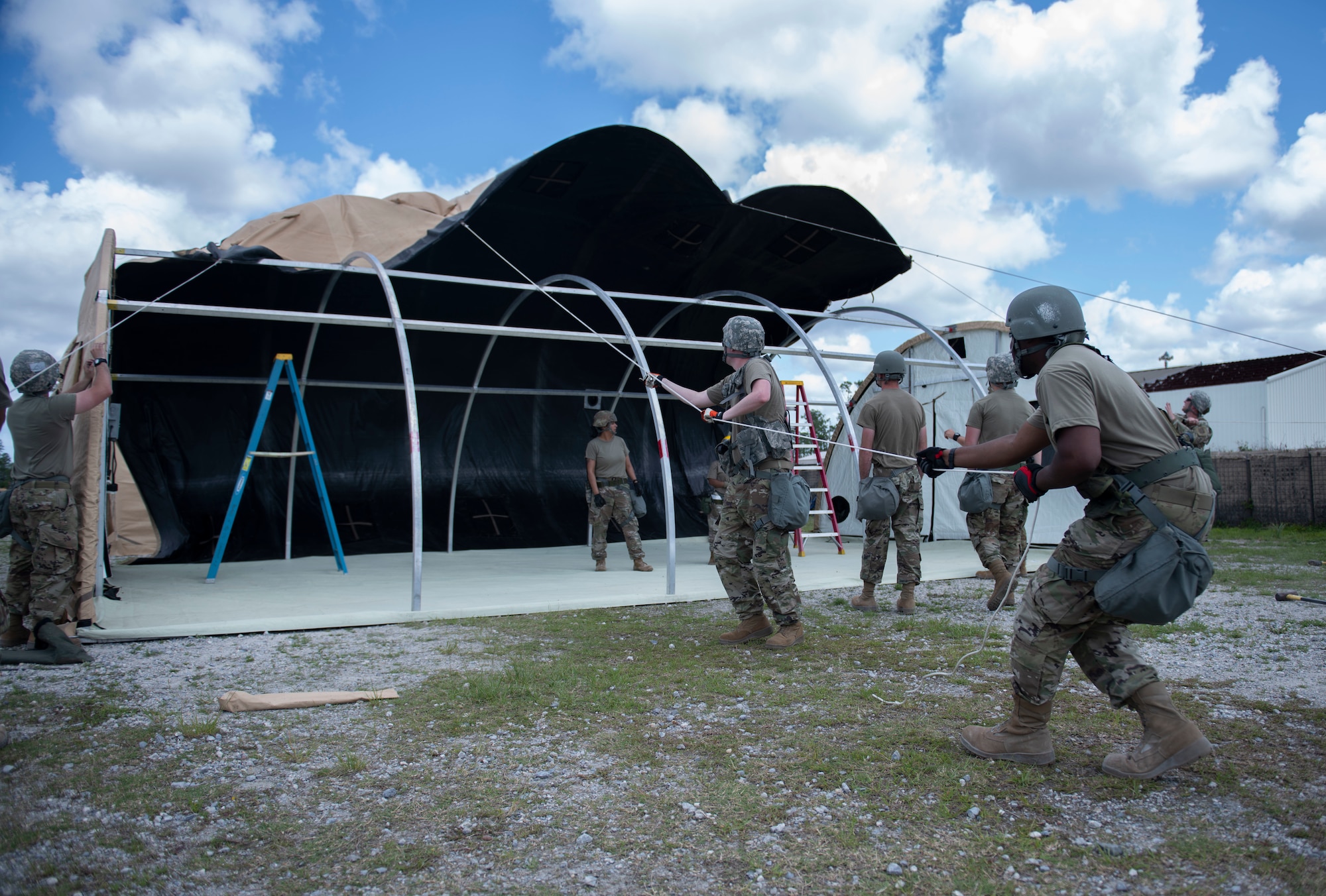 Airmen pull a rope to put up a tent.