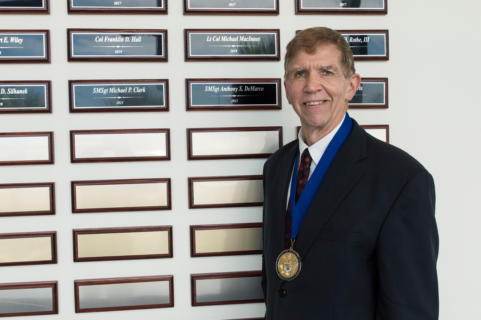 Retired Air Force Senior Master Sgt. Mike Clark poses in front of his plaque after his induction into the Air Force Technical Applications Center's Wall of Honor May 26, 2021.  Clark was one of three inductees who were honored at a ceremony held at the nuclear treaty monitoring center to recognize his contributions to AFTAC's long range detection mission.  (U.S. Air Force photo by Matthew S. Jurgens)
