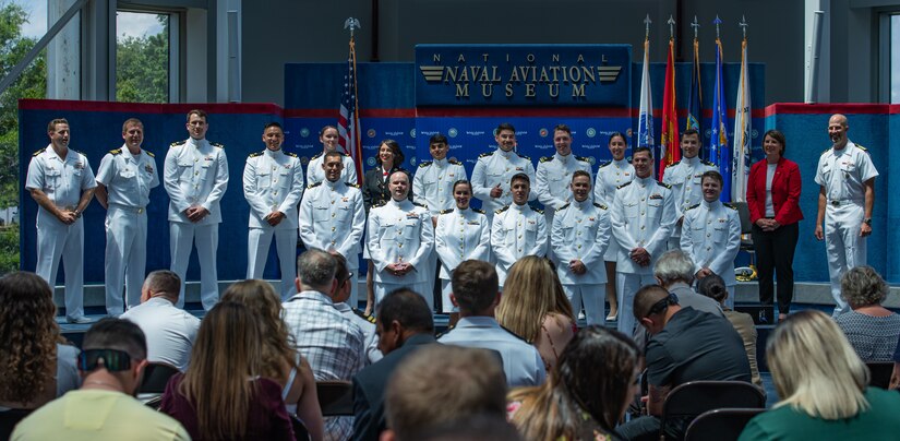 Service members stand in two rows for a photo at an outdoor ceremony in front of an audience.