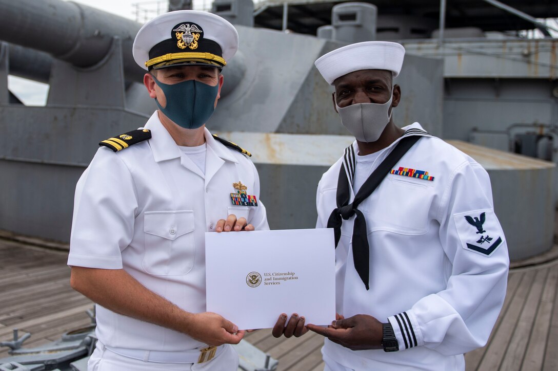 A sailor receives a certificate of naturalization from Lt. Andrew Decker during a naturalization ceremony aboard the Japanese Memorial Ship Mikasa.