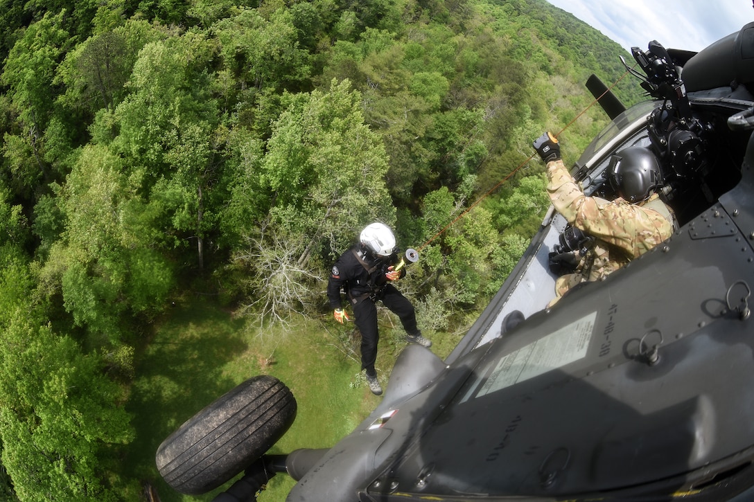 A  National Guardsman holds on to a pulley from a hovering helicopter.