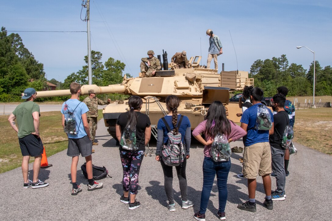 A group of kids stand and listen to soldiers on a tank.
