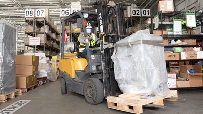 Man on a forklift moves a pallet of supplies in a warehouse with shelves and boxes.