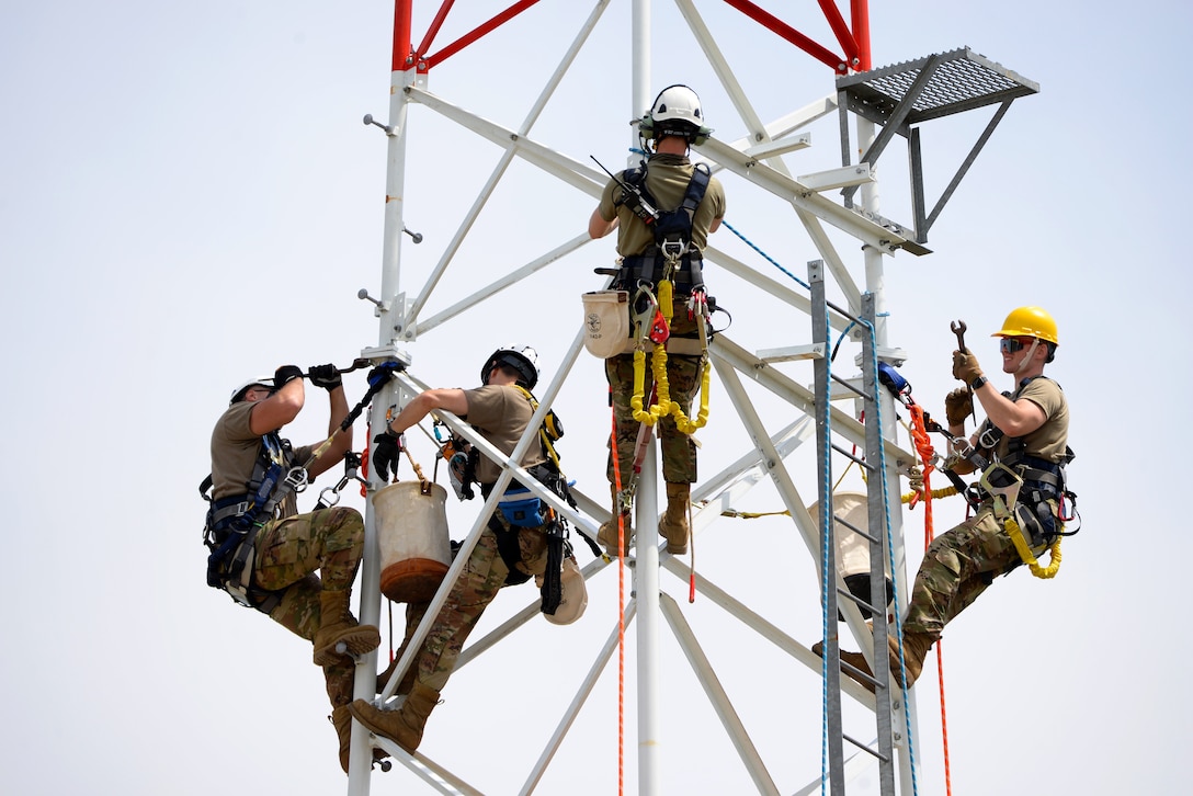 Airmen climb a radio tower while holding tools.
