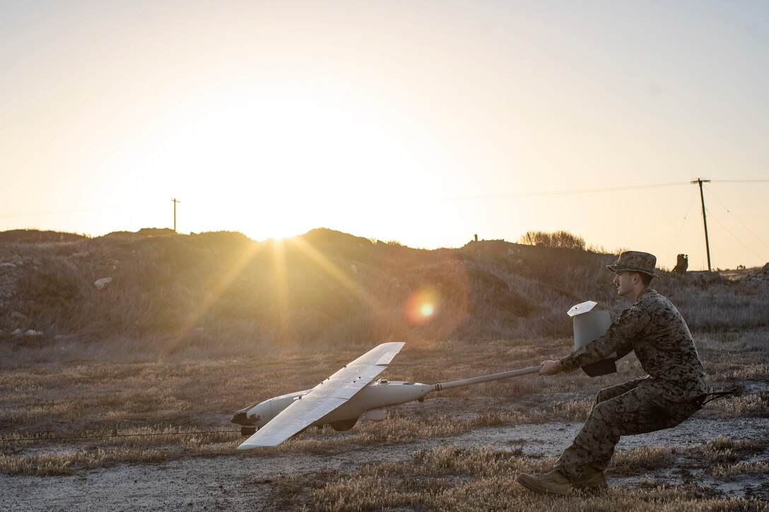 A Marine launches an unmanned aerial system in a field under a sunlit sky.