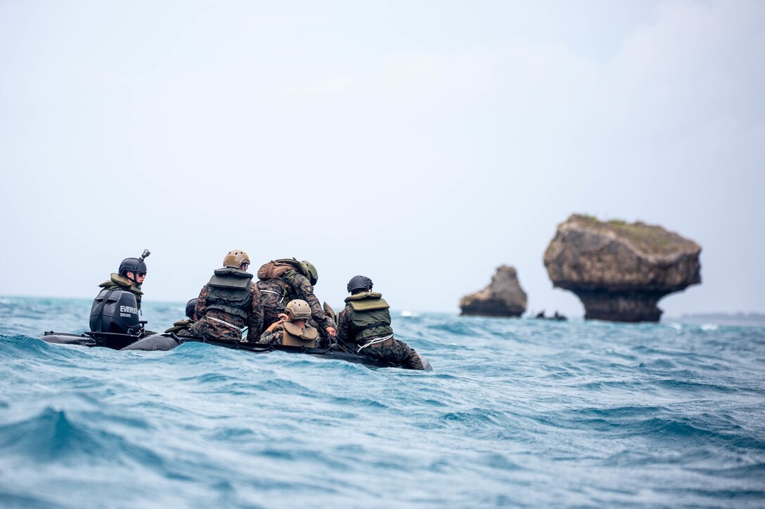 Marines ride in a small boat near rocks.
