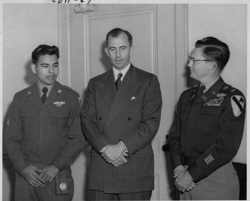 Three men stand side by side with their hands folded beneath their waists.