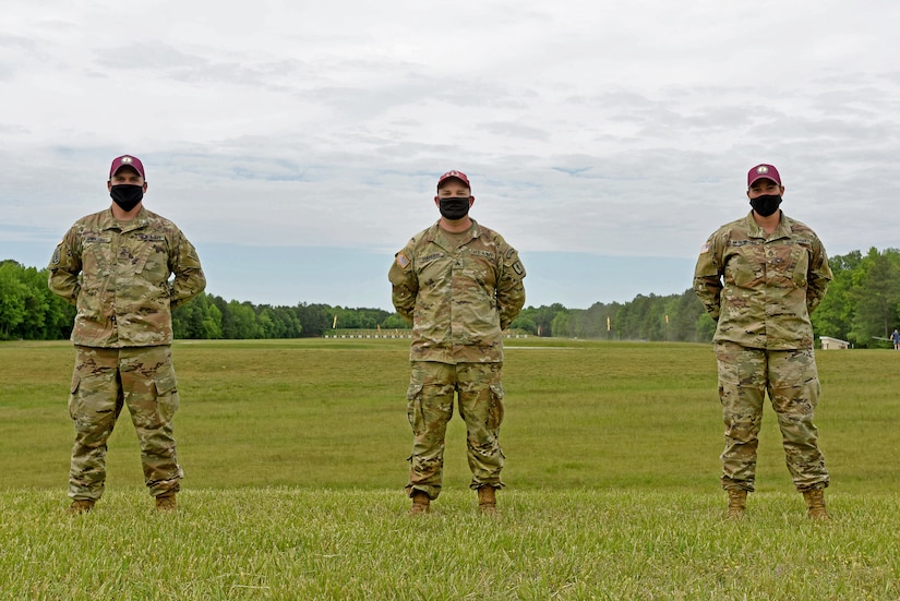 Three soldiers stand for a photo in a green field.