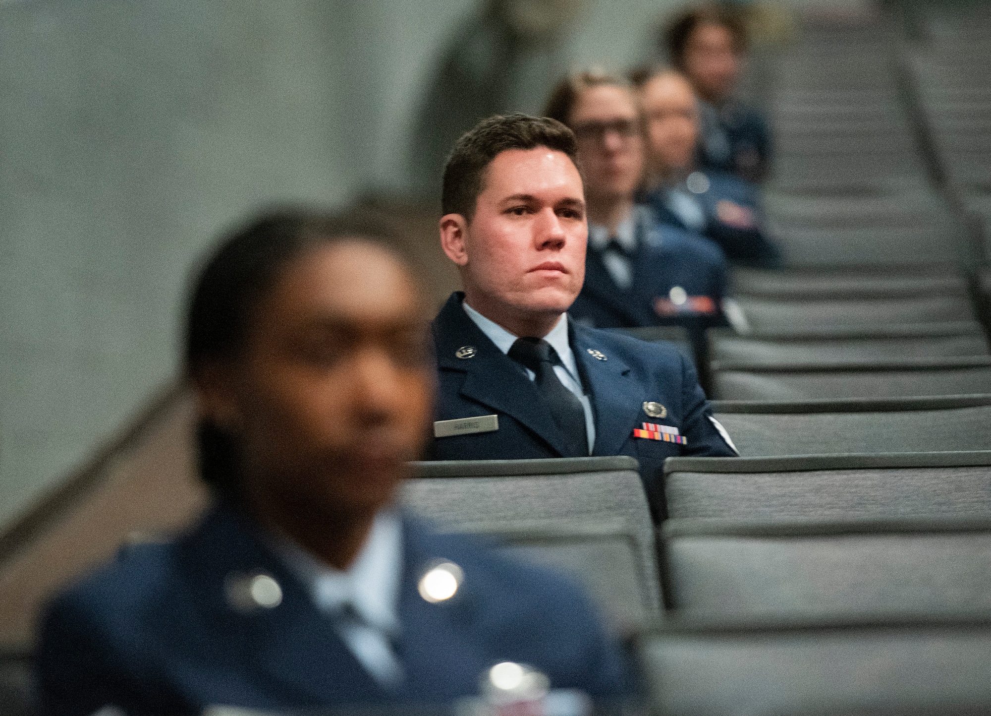 Staff Sgt. Nicholas Harris-Duke, National Air and Space Intelligence Center, listens with other graduates to the commencement address during the Community College of the Air Force spring graduation ceremony May 26, 2021, in the theater at Wright-Patterson Air Force Base, Ohio. Harris-Duke earned an associate’s degree in intelligence studies and technology. (U.S. Air Force photo by R.J. Oriez)