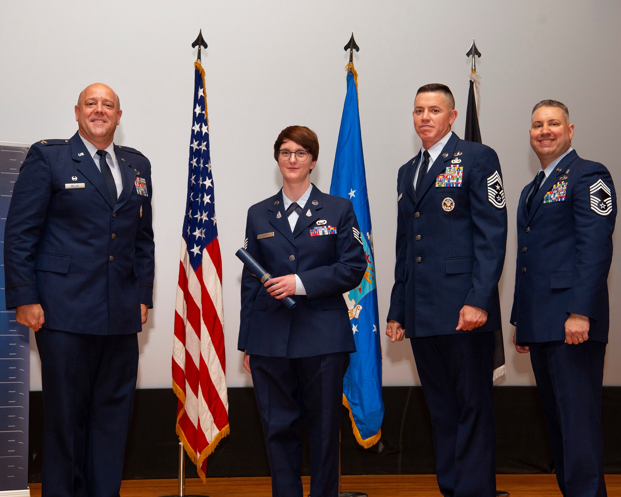 U.S. Space Force Sgt. Donna Farris, 73rd Intelligence, Surveillance and Reconnaissance Squadron, poses with (from left) Air Force Col. Patrick Miller, 88th Air Base Wing and installation commander; Chief Master Sgt. Jason Shaffer, 88 ABW command chief; and Chief Master Sgt. Erik Robbins, U.S. Air Force School of Aerospace Medicine’s Occupational and Environmental Health Division superintendent, as she receives her diploma May 26, 2021, during the Community College of the Air Force spring graduation ceremony in the theater at Wright-Patterson Air Force Base, Ohio. Farris was one of 57 Airmen and Guardians who earned degrees. (U.S. Air Force photo by R.J. Oriez)