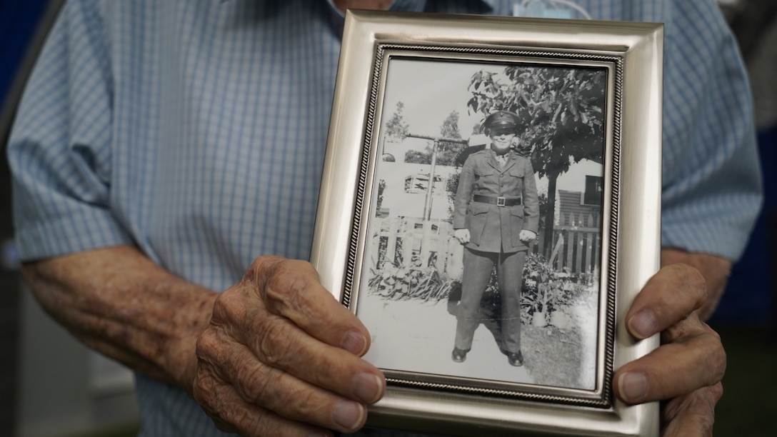 Ninety-Eight-year-old World War II Marine Corps Veteran Donald Folsom, who served in Tarawa, Saipan, Tinian, and Okinawa as a cannoneer with the 2nd Marine Division, poses with a photo from his time in service after the U.S. Marine Corps Silent Drill Platoon performed at St. Joe's Sports Dome in support of Recruiting Station (RS) Cleveland and RS Lansing, June 1, 2021. After each performance they conducted a meet and greet with the audiences, poolees and recruiters. (U.S. Marine Corps photo by Sgt. Jason A. Kolela)