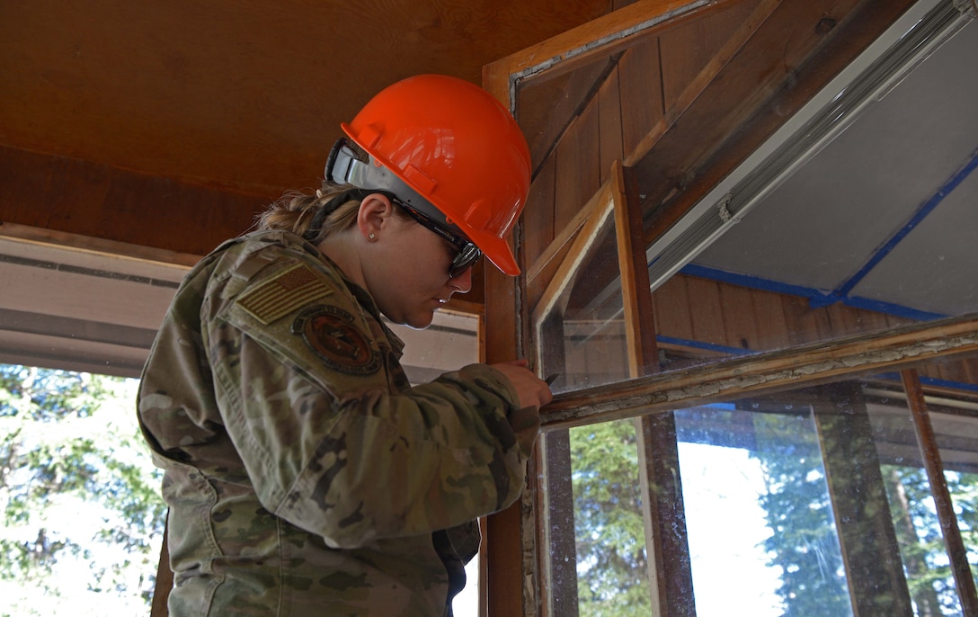 U.S. Air Force Capt. Kathryn Iden, the 354th Civil Engineer Squadron Command Support Staff section commander, removes old sealant on a window during a troop training project May 26, 2021, at the Birch Lake Military Recreation Area, Alaska. During projects like this, troops execute 96-hour contingency training which usually involves fixing up a small building or a few playgrounds, but this year the project was significantly larger with approximately 135 Airmen from the squadron participating and over $86,000 of construction and repairs completed. (U.S. Air Force photo by Senior Airman Beaux Hebert)
