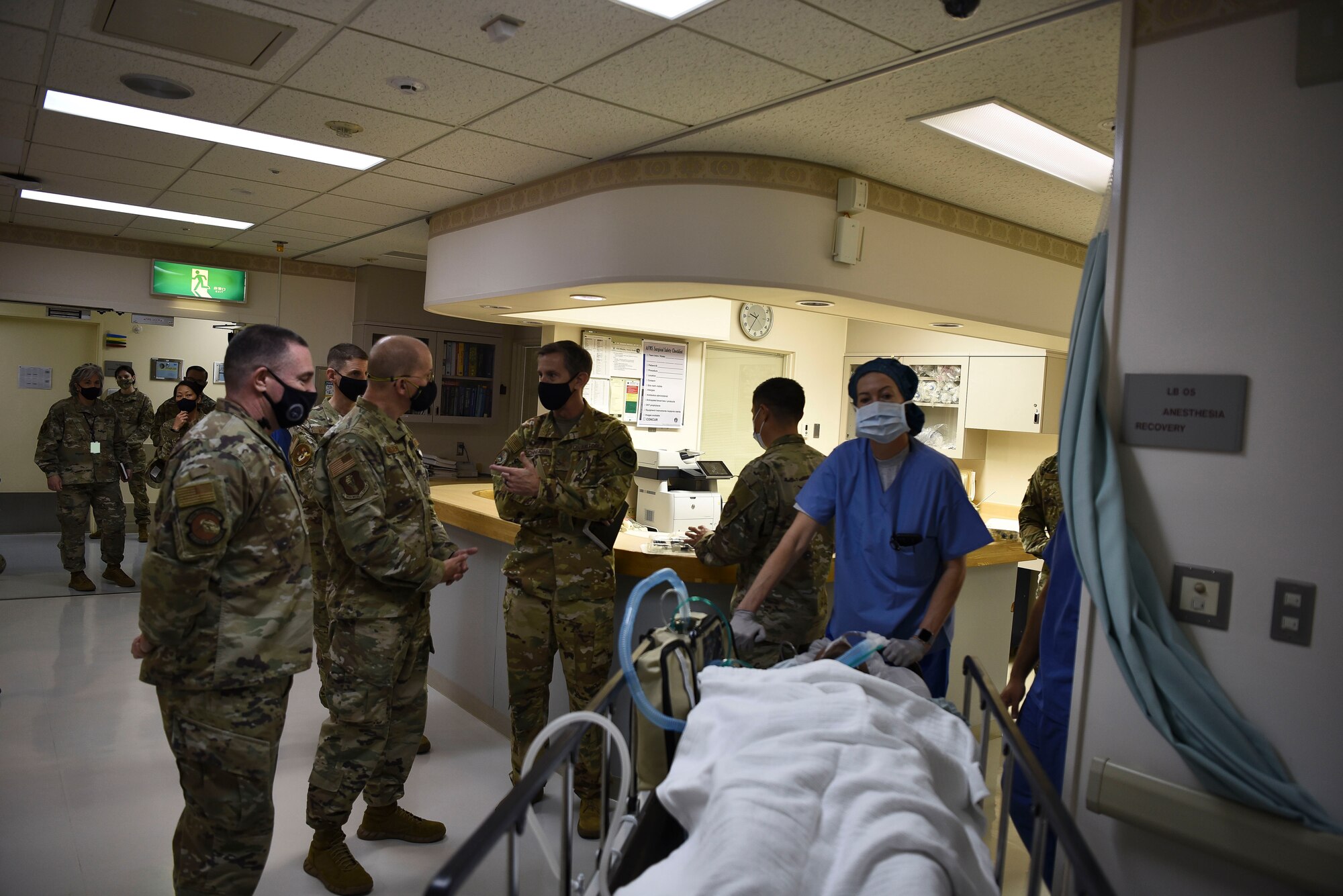A nurse wheels a person past military members in a hospital.