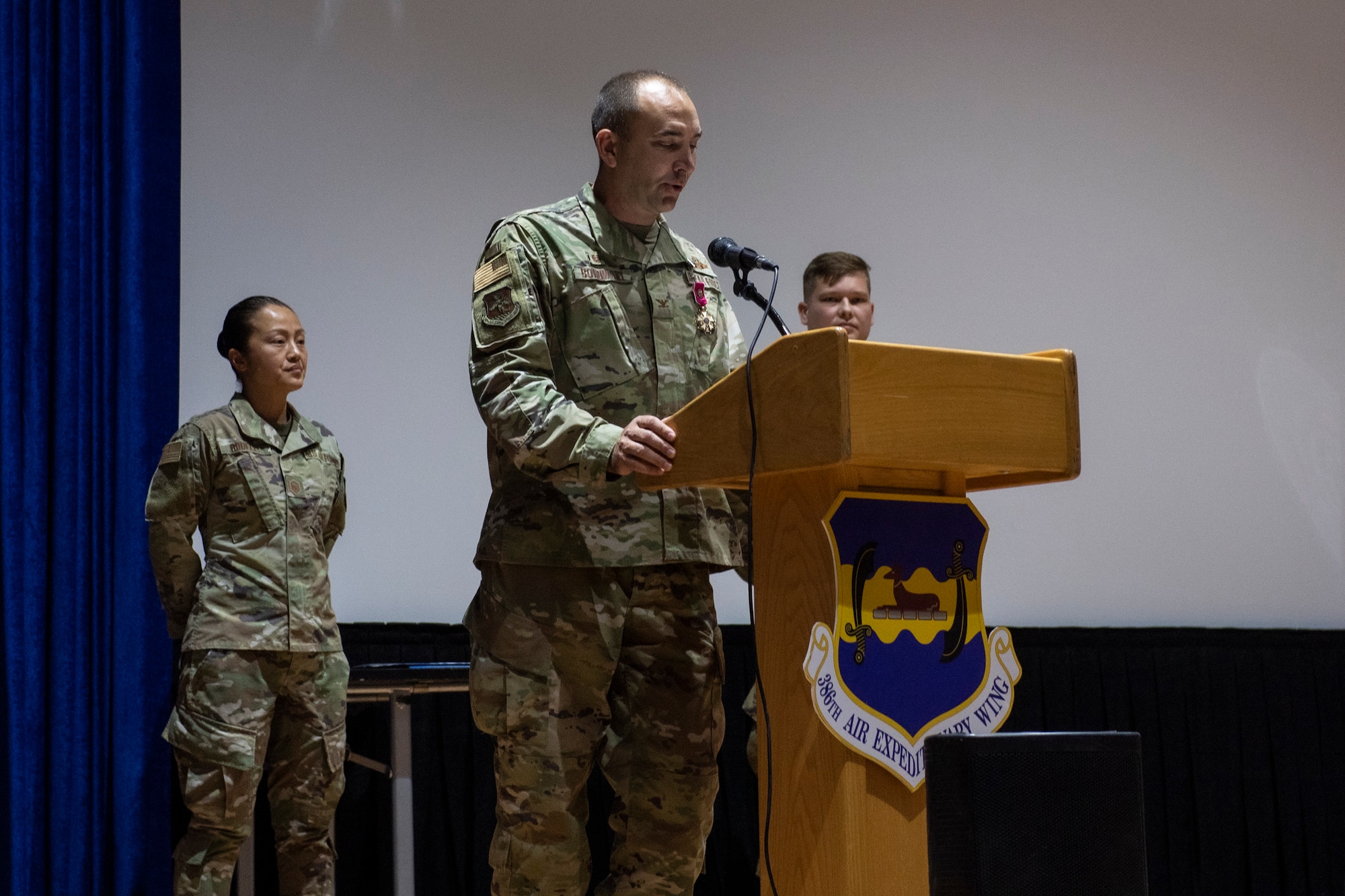 Man in uniform speaks standing behind a podium on stage.