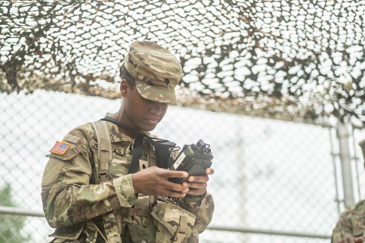 A woman dressed in a military uniform operates a radio.