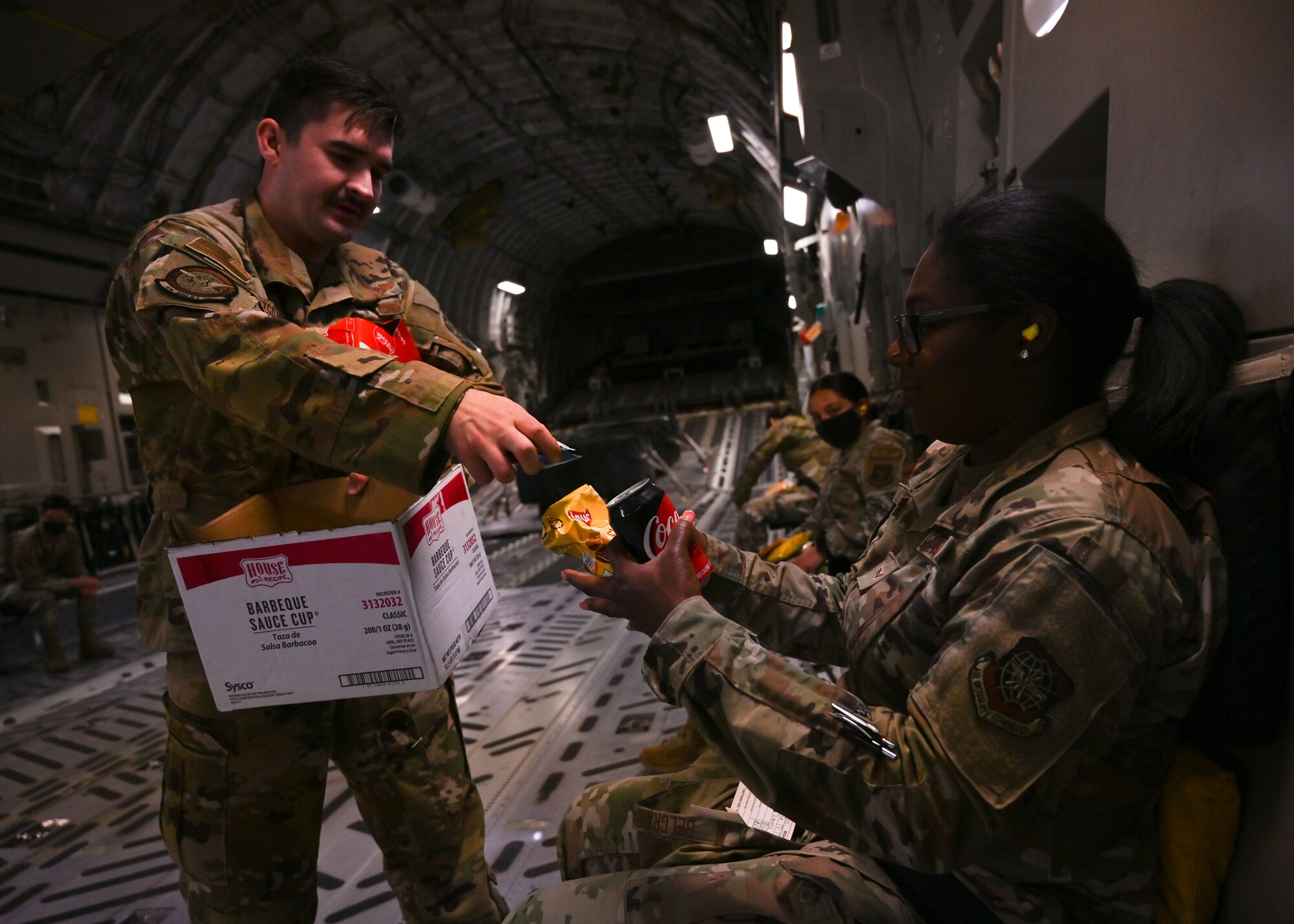 U.S. Air Force Staff Sgt. Ian Bertsch-Huber, 4th Airlift Squadron loadmaster, gives Airman 1st Class Imani Belgrave, 627th Force Support Squadron command support staff member, an inflight lunch on a C-17 Globemaster III at Joint Base Lewis-McChord, Washington, June 2, 2021. Belgrave participated in an orientation flight as part of the Airmen Experience, a two-day immersive program that connects Airmen to the mission, allowing them to see firsthand how their role contributes to the bigger picture at JBLM. (U.S. Air Force photo by Airman 1st Class Callie Norton)