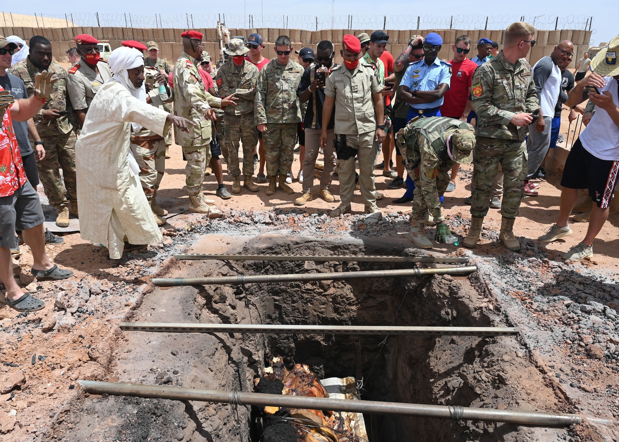 American military members listen to instructions on raising the cooked camel from an underground oven at Nigerien Air Base 201, Agadez, Niger, May 31, 2021. The feast demonstrated the shared commitment of Nigeriens and Americans to counter terrorism, sustain peace, and enhance security in the Sahel.