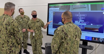 PENSACOLA, Fla. (August 20, 2020) Rear Adm. Pete Garvin (center), commander, Naval Education and Training Command (NETC), discusses the Multipurpose Reconfigurable Training System 3D® (MRTS 3D®) technology training device with staff at Information Warfare Training Command (IWTC) Corry Station. Garvin, along with NETC Force Master Chief Matthew Harris, visited for a familiarization brief and tour of the Center for Information Warfare Training (CIWT) and IWTC Corry Station onboard Naval Air Station Pensacola Corry Station, Pensacola, Florida. The visit offered an opportunity to update them on CIWT / IWTC Corry Station training and development approaches for building a talented fleet through initiatives, such as Ready, Relevant Learning, that take recruits from "street to fleet" and transform civilians into highly skilled, operational, and combat-ready information warfare warfighters.