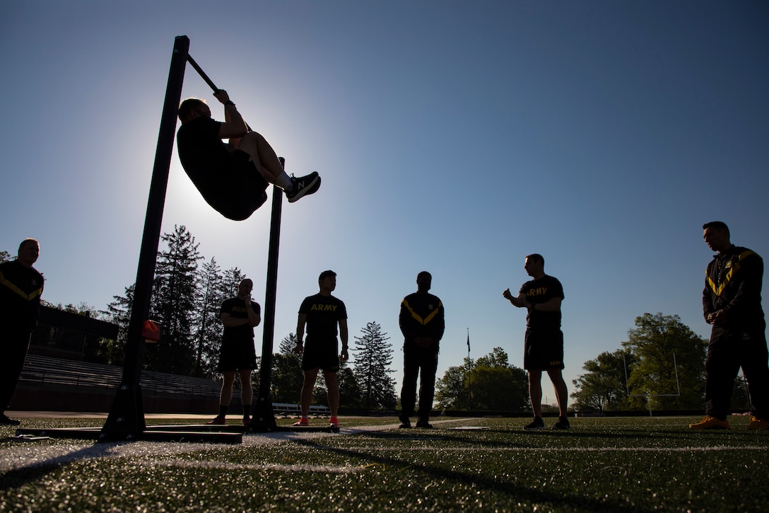 A soldier shows fellow soldiers how to perform a leg tuck as show in silhouette.