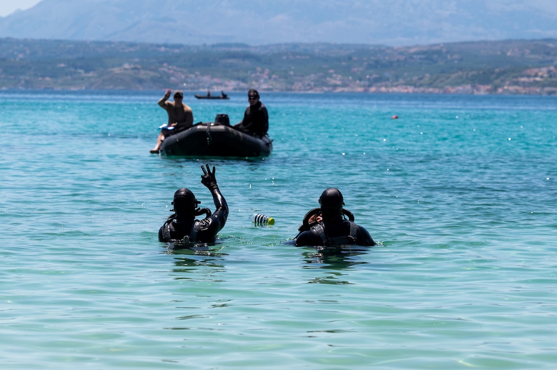 Sailors and airmen swim near a small boat in a body of water.