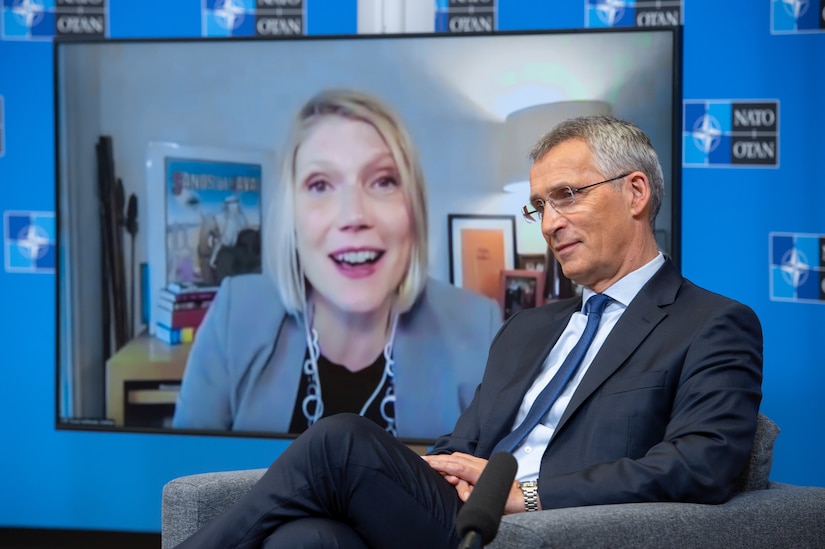 A man sits in a chair answering questions from a woman on a screen.