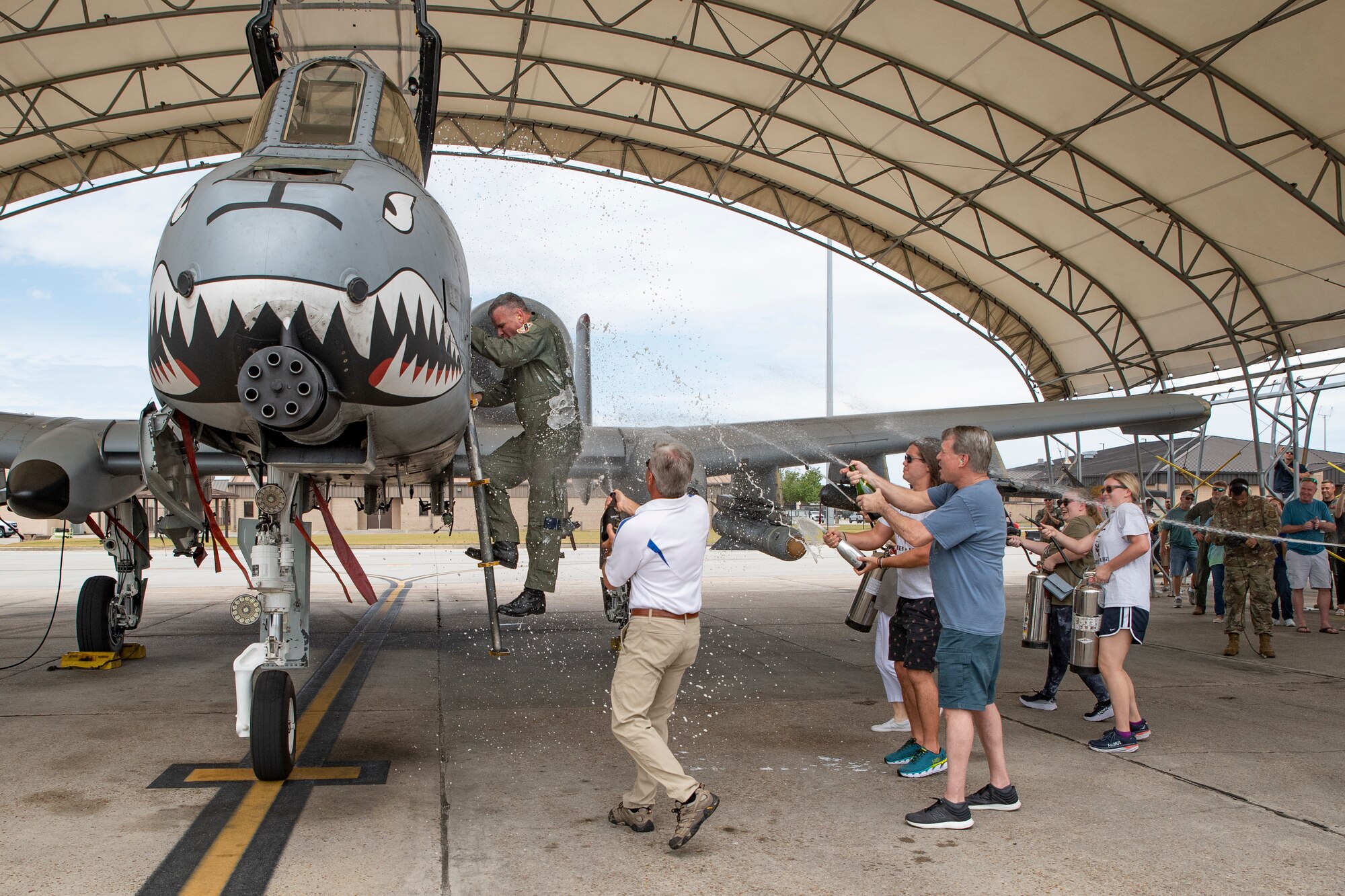 A photo of  Lieutenant Colonel Rob Sweet climbing out of an aircraft as his friends and family spray him with champagne