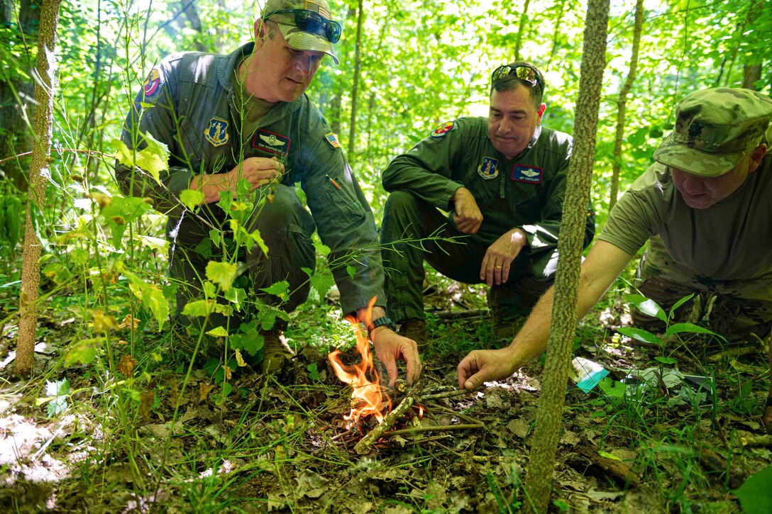 Three guardsmen build a small fire in a wooded area.