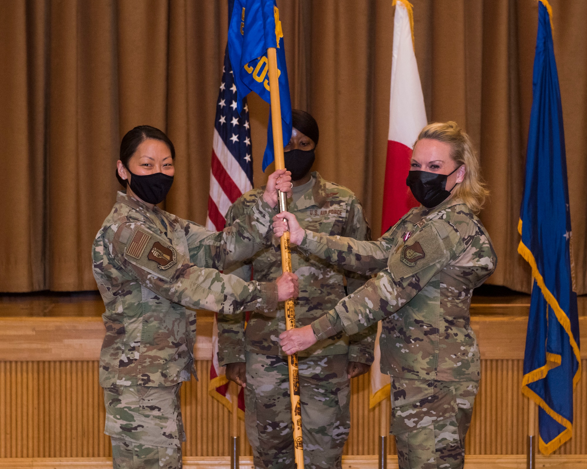 Women in uniform pose for a photo while holding a guidon.