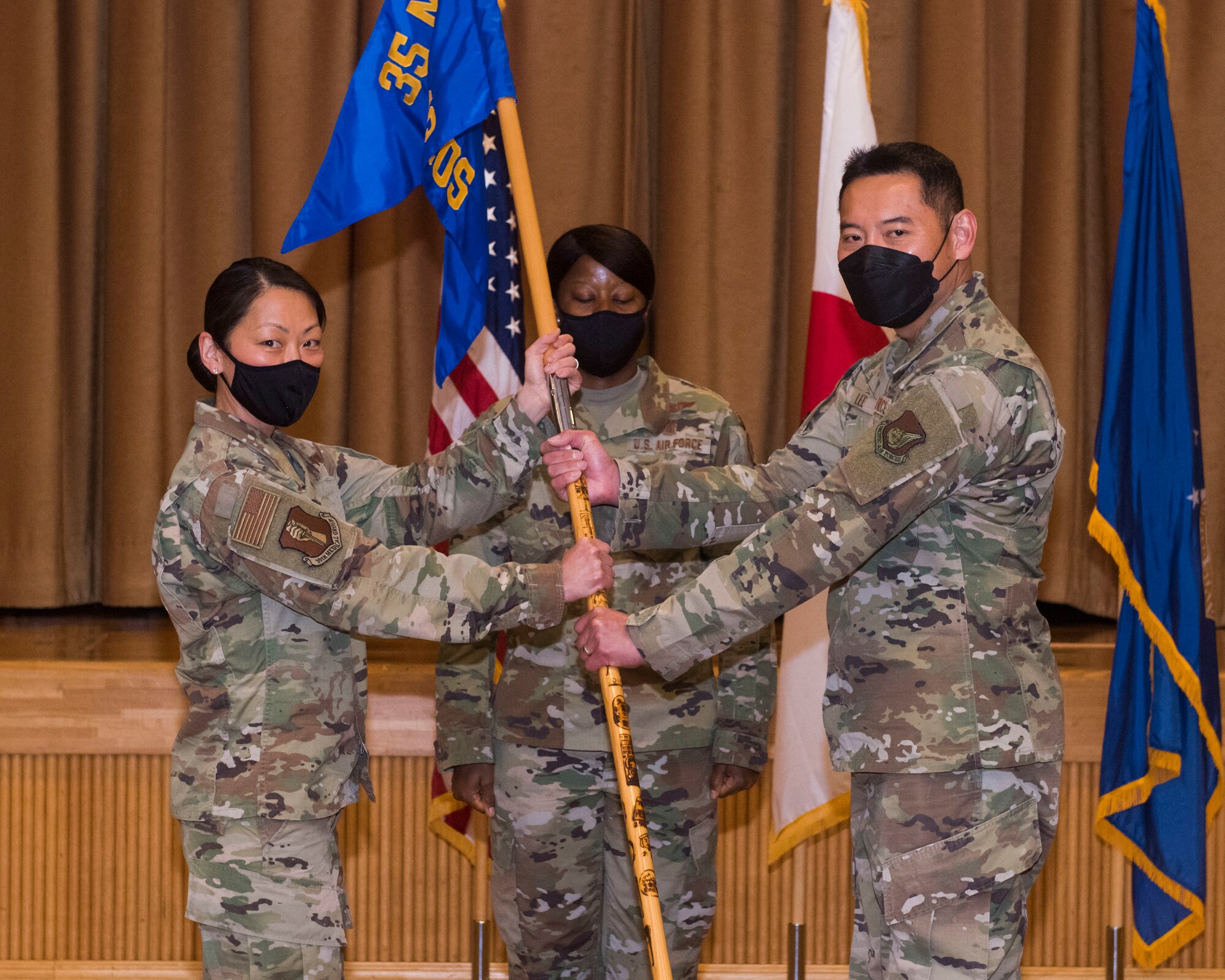 Men and women in uniform pose for a photo while holding a guidon.