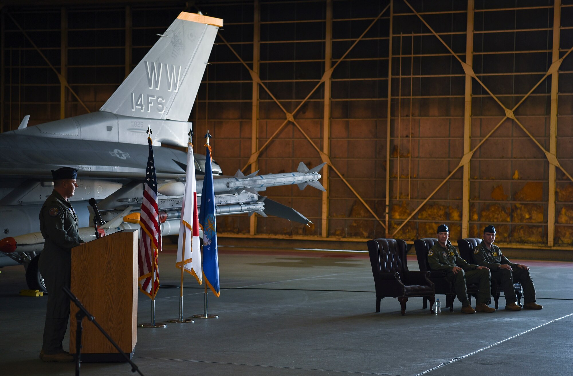 A uniform man behind a podium looks at two other uniformed members in seats.
