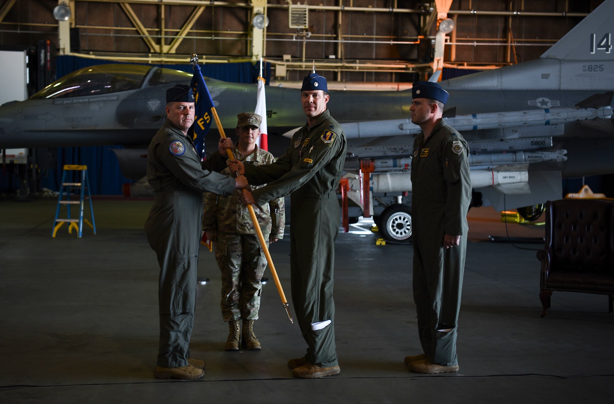 Two uniformed men hold a flag while other uniformed members stand in the position of attention.