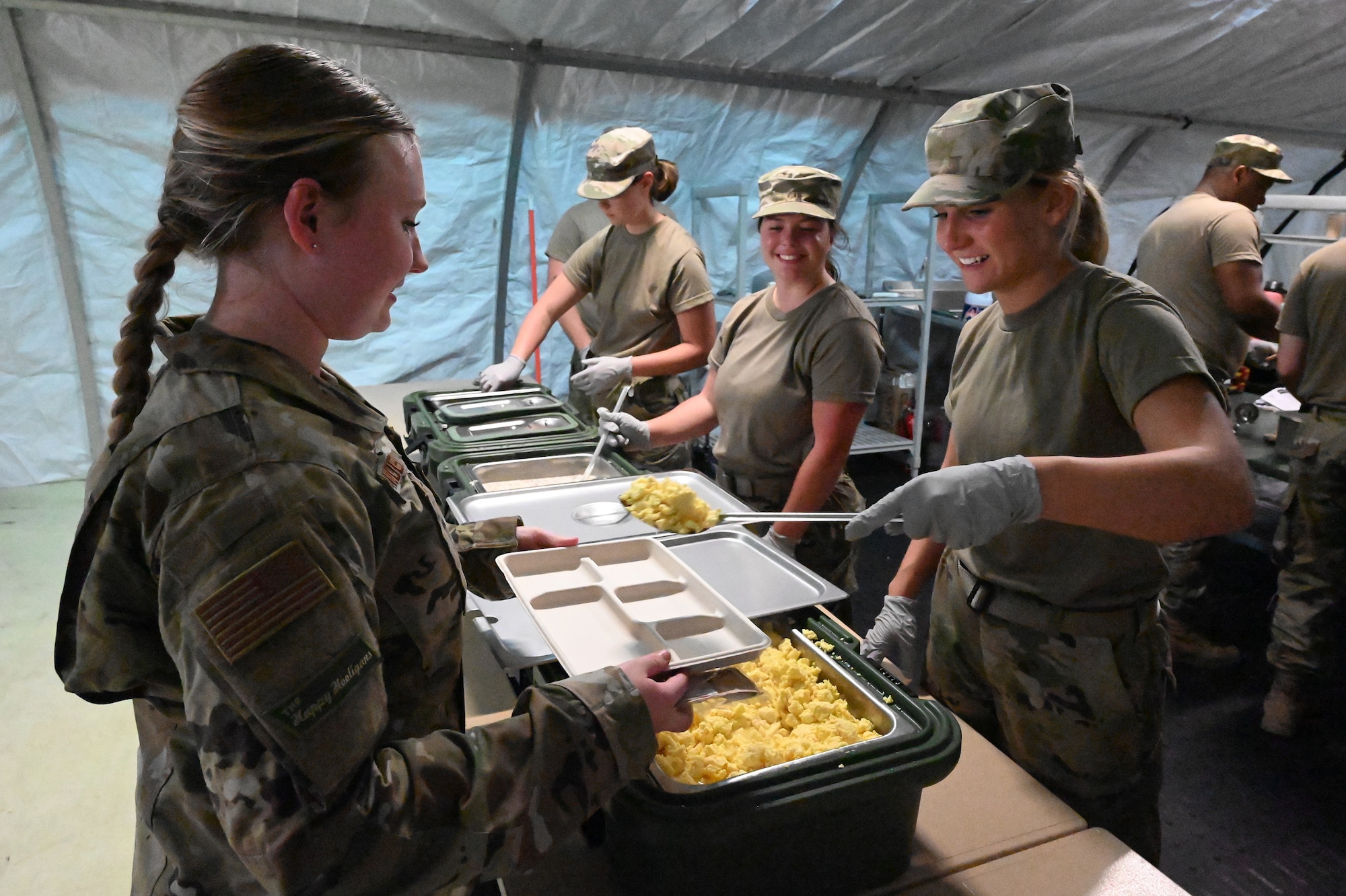 Three female military members dish food onto a tray inside a tent for another female military member at the North Dakota Air National Guard Base, Fargo, N.D., June 4, 2021.