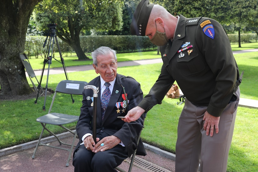 A man in military uniform hands a veteran a coin during a memorial ceremony.