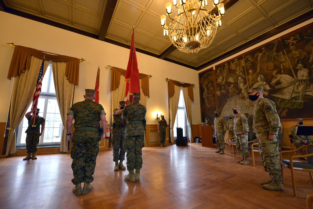 U.S. Marine Corps Sgt. Maj. Aaron G. McDonald, command sergeant major of U.S. Marine Corps Forces, Europe and Africa (MARFOREUR/AF), hands the organizational colors to outgoing commander Maj. Gen. Michael E. Langley during the MARFOREUR/AF change of command ceremony at the U.S. Army Garrison Stuttgart firehouse in Boeblingen, Germany, May 6, 2021. This ceremony recognizes the significance of the passage of command, honors the accomplishments of the organization under the outgoing commander, and formally appoints the incoming commander. (U.S. Army Photo by Jason Johnston)