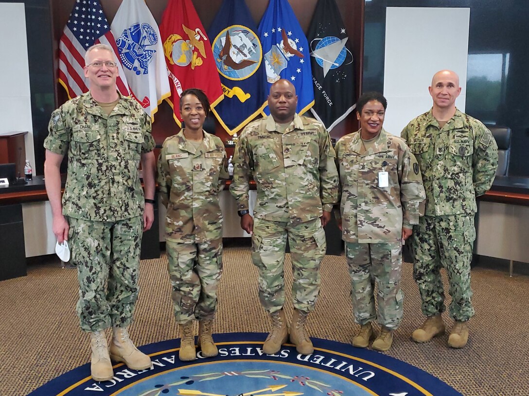 Four service members stand for a photo with flags in the background