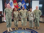 Four service members stand for a photo with flags in the background