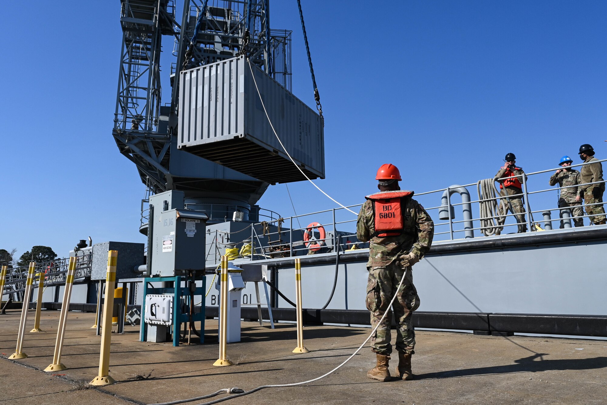 U.S. Soldiers from the 7th Transportation Brigade (Expeditionary) move shipping crates at 3rd Port, Joint Base Langley-Eustis, Virginia, March 9, 2021. The crates were loaded by crane onto a waiting barge to be transported to an exercise. (U.S. Air Force photo by Senior Airman Sarah Dowe)