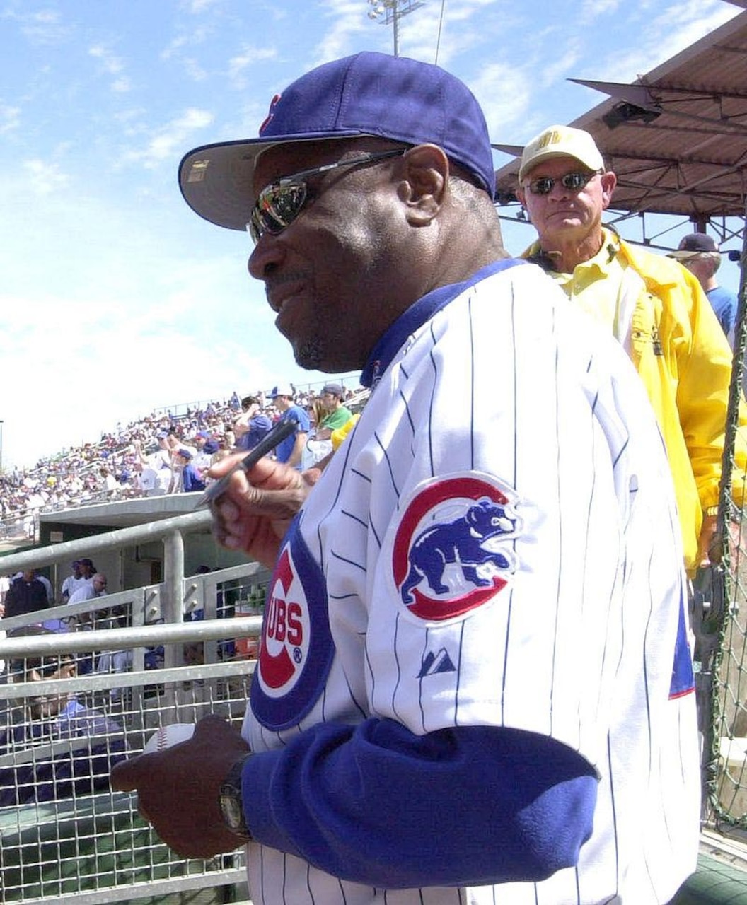 A man in a baseball uniform looks out over a baseball field from the stands.